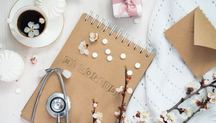 A photo showing a stethoscope, medicines, a cup of coffee, and a writing pad mentioning 'menopause'. — Canva