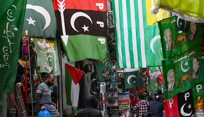 People walk past flags of political parties displayed for sale at a market in Lahore ahead of the February 8 general elections. — AFP