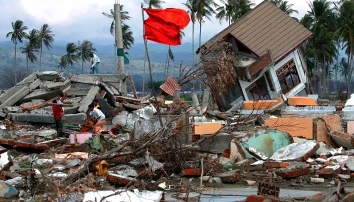 Achenese men walk amid the debris of their devastated houses on the outskirts of Banda Aceh following the 2004 tsunami. — Reuters/File