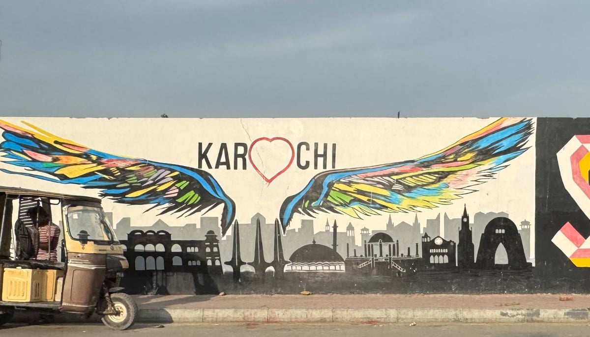 A rickshaw is parked near a street side with a wall in the backdrop displaying graffiti of Karachis popular sites and monuments. — Photo by author