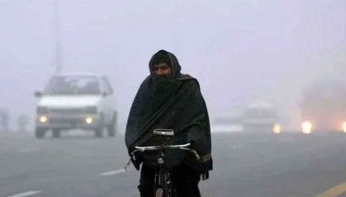 A man wrapped in shawl cycles on a road in cold weather. — AFP/File